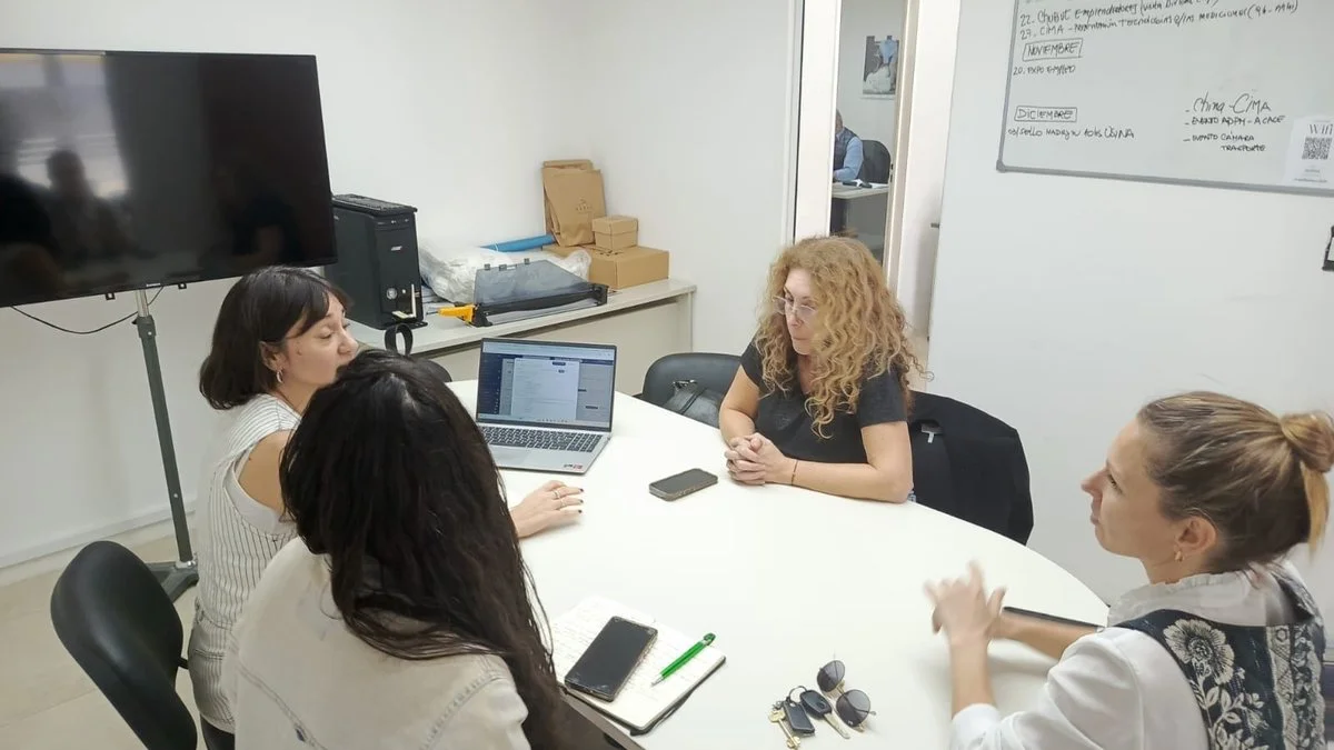Cuatro mujeres conversan alrededor de una mesa de reuniones con una computadora portátil y un teléfono sobre la mesa.