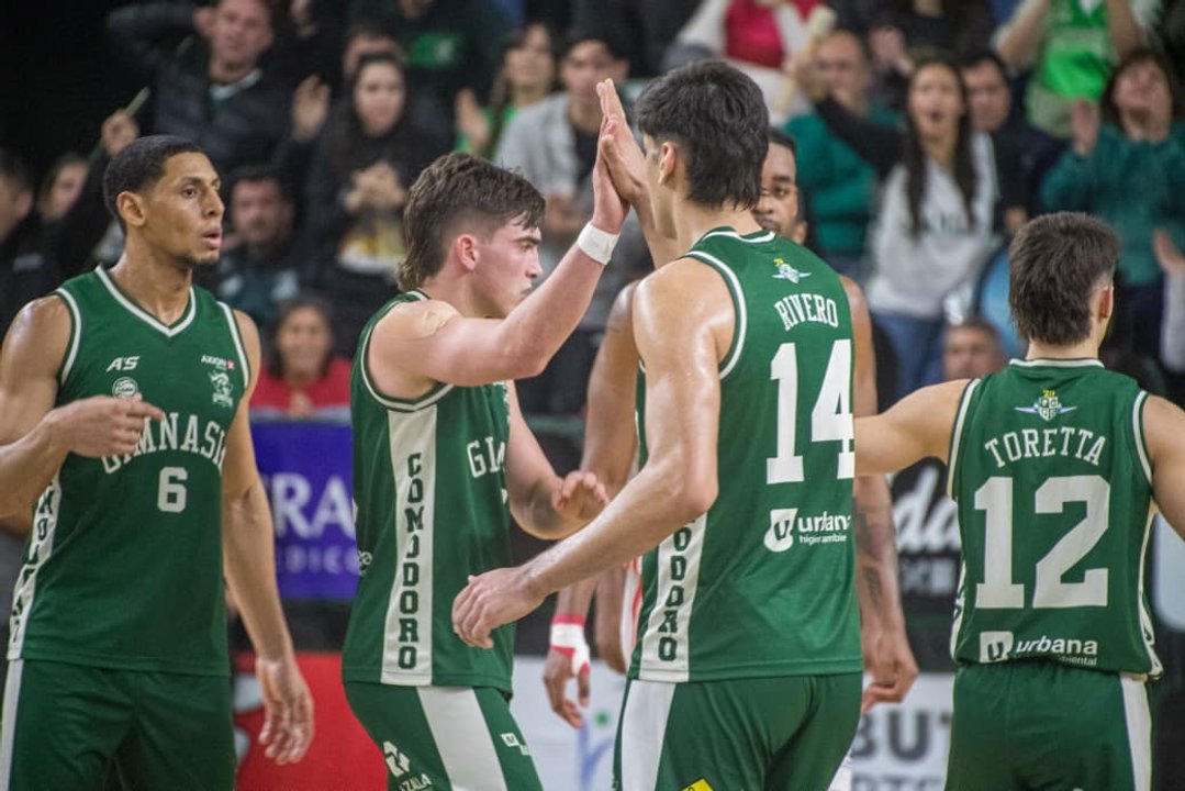 Unos jugadores con camisetas verdes se chocan las manos durante un partido, con público de fondo en la tribuna