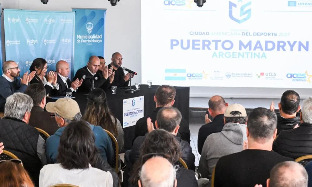 Personas aplauden en una mesa frente a una pantalla con el texto Puerto Madryn.