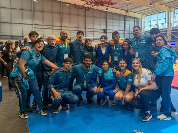 Un grupo de deportistas con buzos celestes posa sonriente sobre una colchoneta azul en un gimnasio.