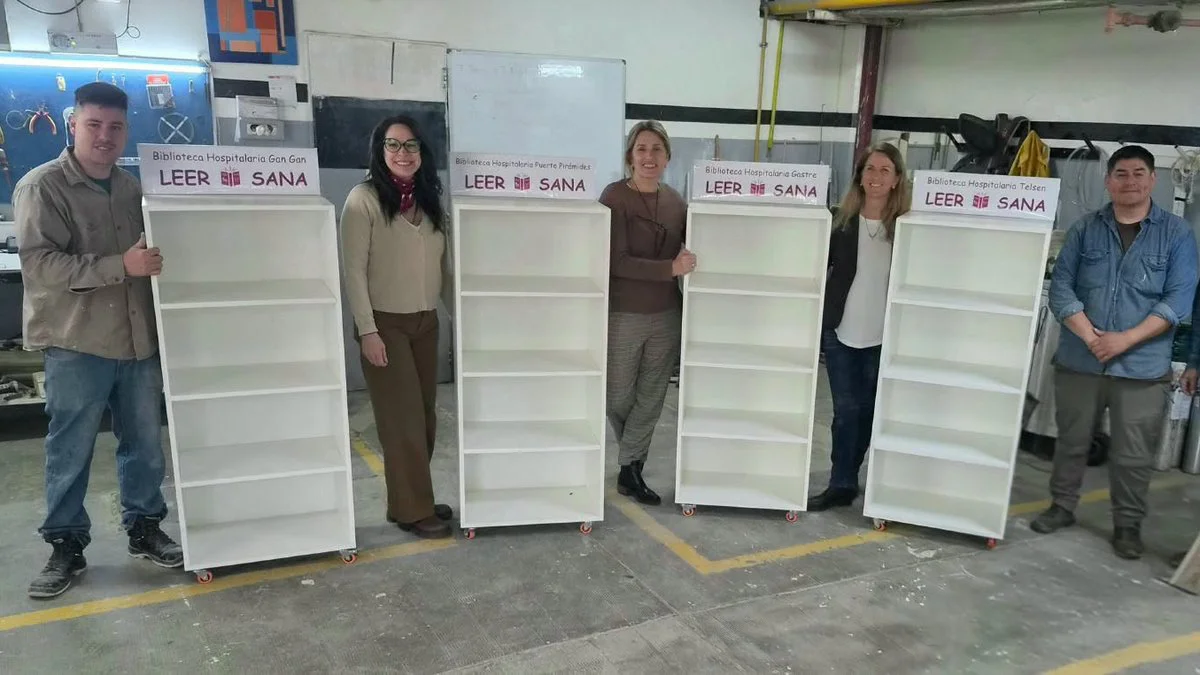 Unos adultos posan junto a estanterías blancas con carteles de Leer Sana en un taller con paredes grises y herramientas