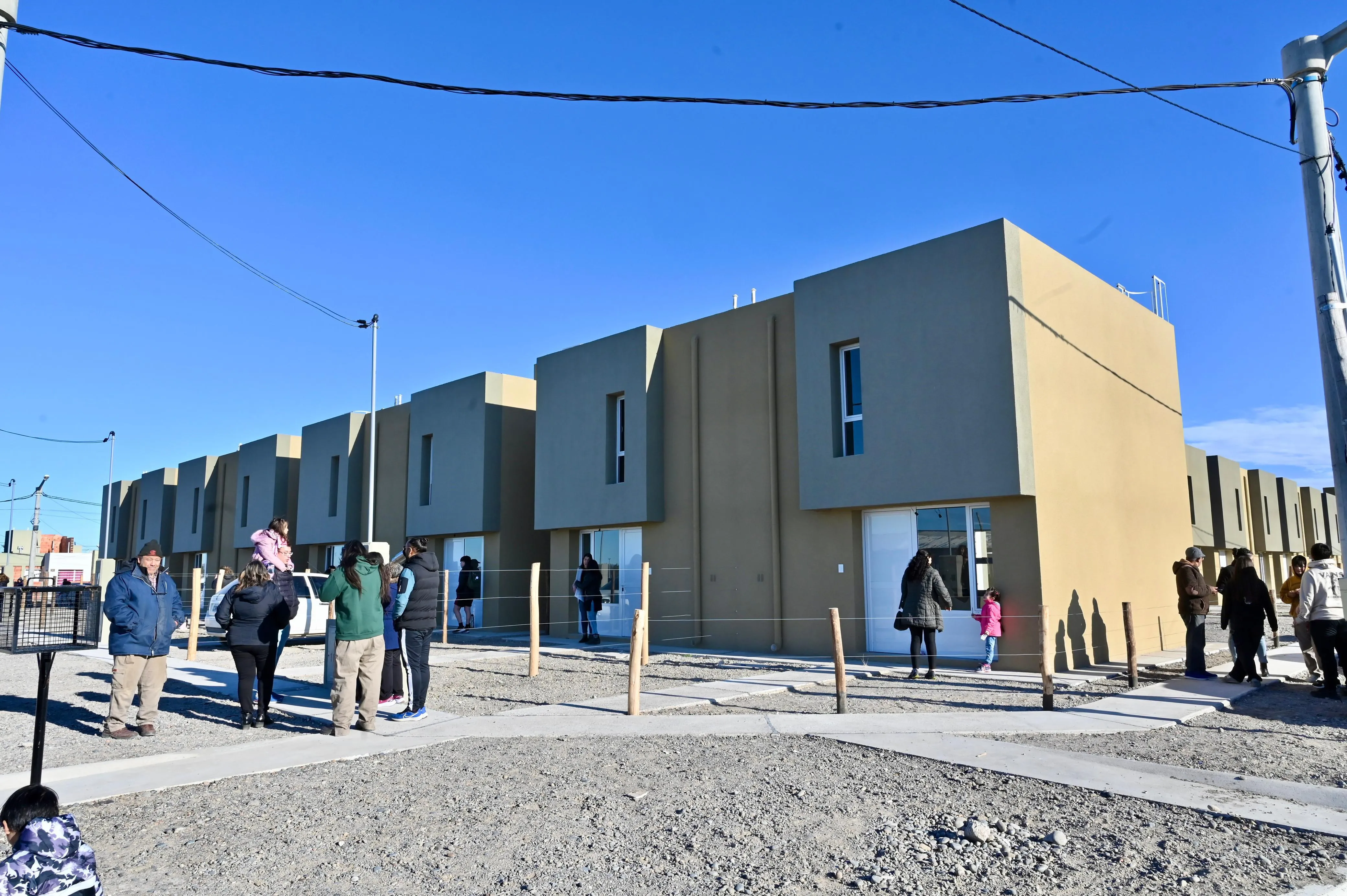 Unas personas recorren frente a casas nuevas de dos pisos con fachadas grises y beige, bajo un cielo celeste.
