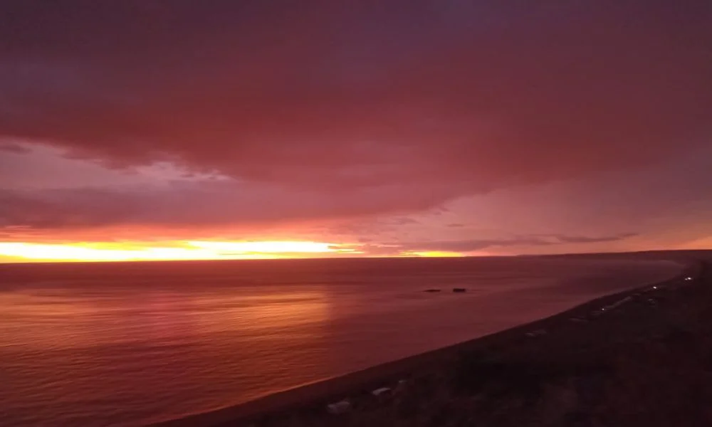 Vista del mar y la costa al atardecer, con el cielo teñido de rojo y naranja