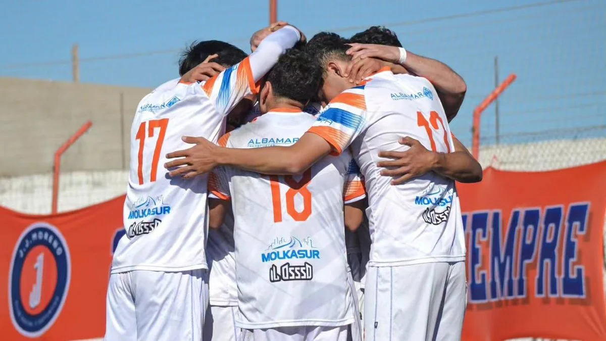 Unos jugadores de camiseta blanca con detalles naranjas se abrazan en círculo frente a un cartel naranja.