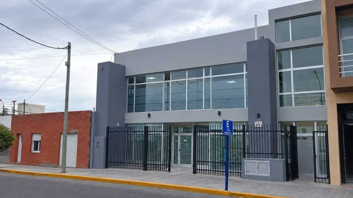 Vista de una fachada gris de dos pisos con ventanales y reja negra, junto a una señal azul de estacionamiento accesible.