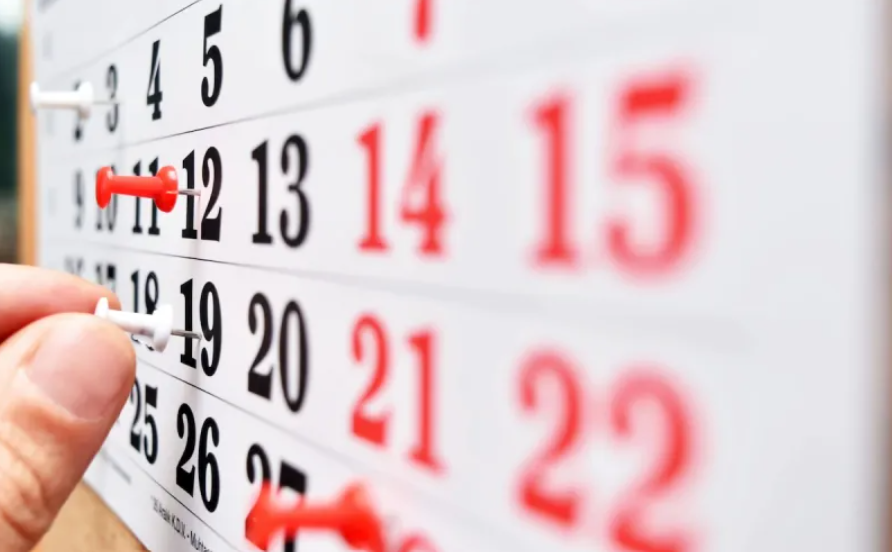Una mano clava chinches rojas y blancas en un calendario de pared con los números en negro y rojo