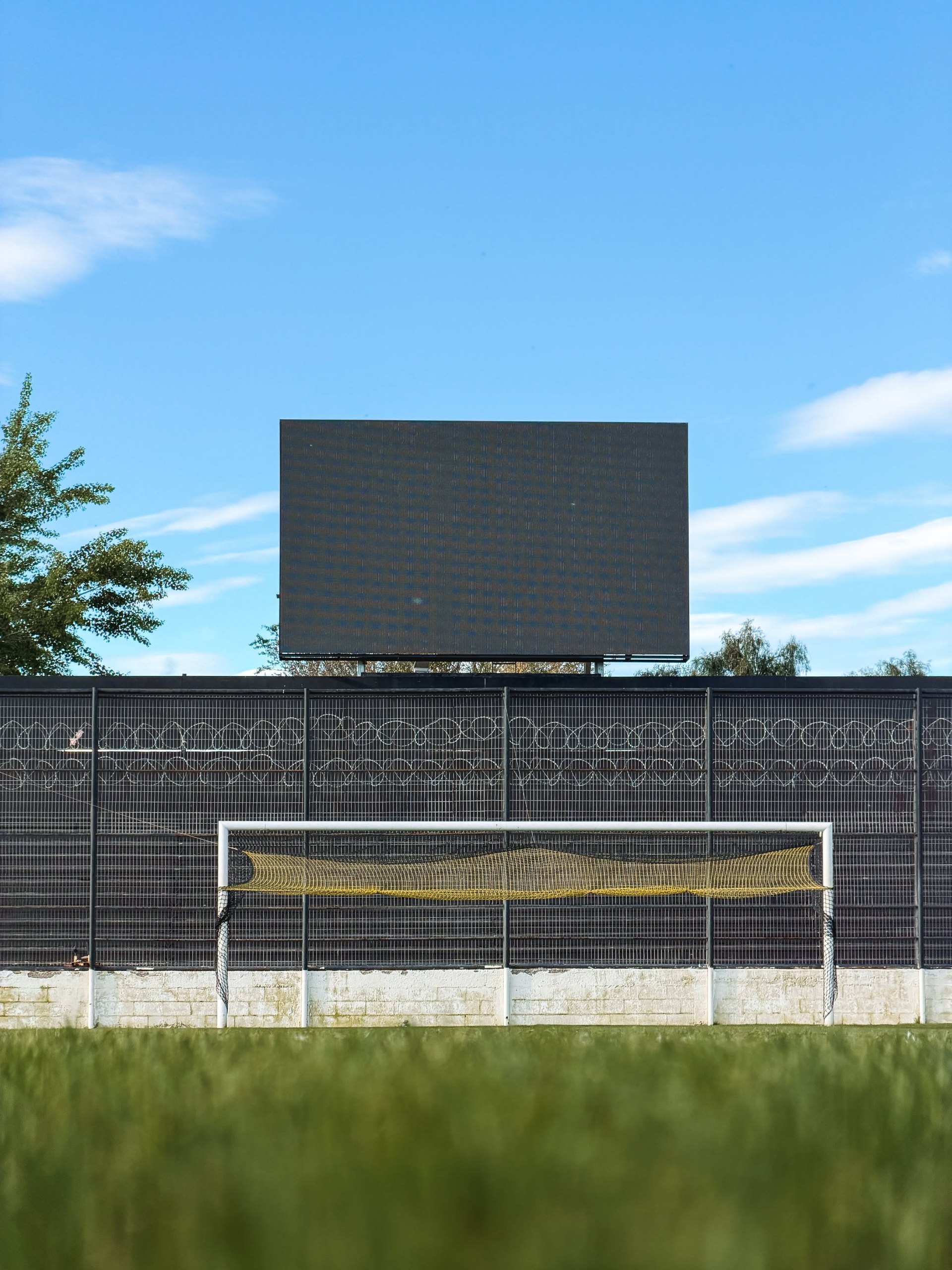 Una pantalla LED apagada se levanta detrás de un alambrado y un arco de fútbol con red amarilla