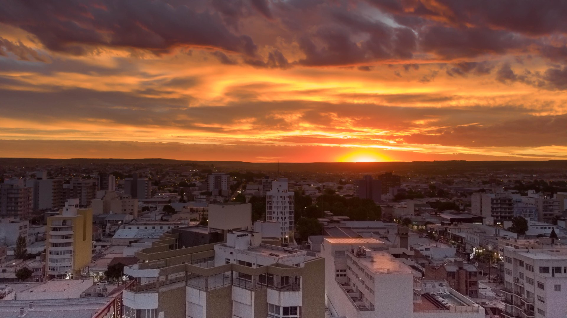 Vista de la ciudad al atardecer, con edificios bajos y un cielo naranja y violeta sobre el horizonte