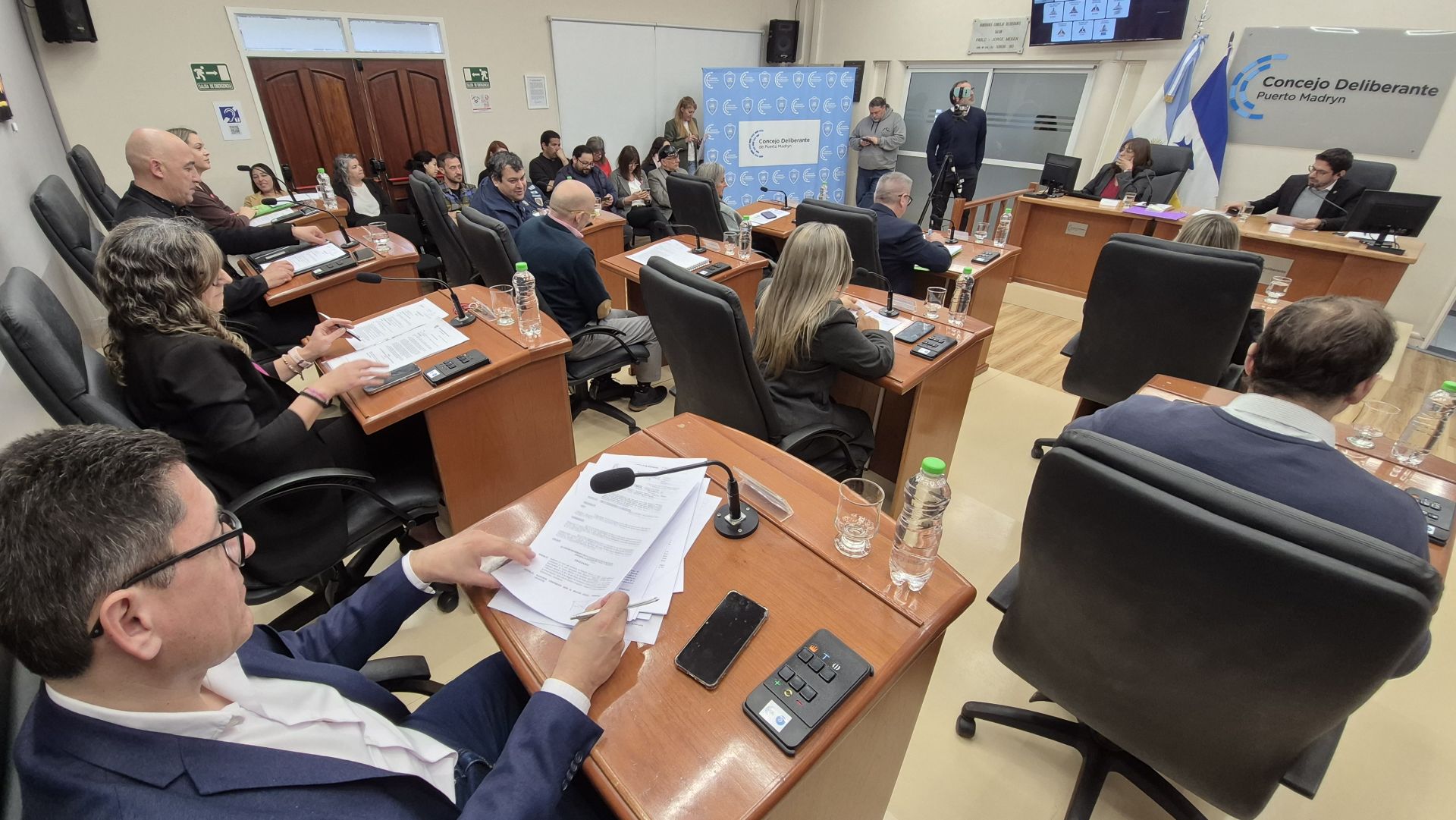 Vista de la sala del Concejo Deliberante con concejales sentados en sus bancas y papeles sobre los escritorios.