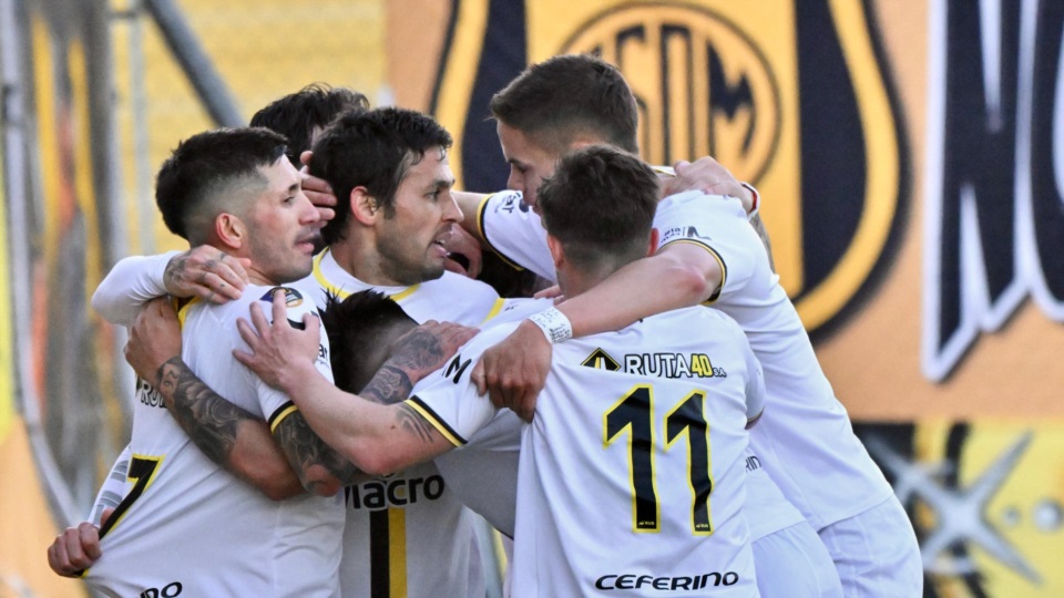 Unos jugadores con camisetas blancas y bordes dorados se abrazan en un festejo.