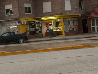 Vista de la fachada de un local con toldo amarillo sobre una calle, con una camioneta negra estacionada al costado.